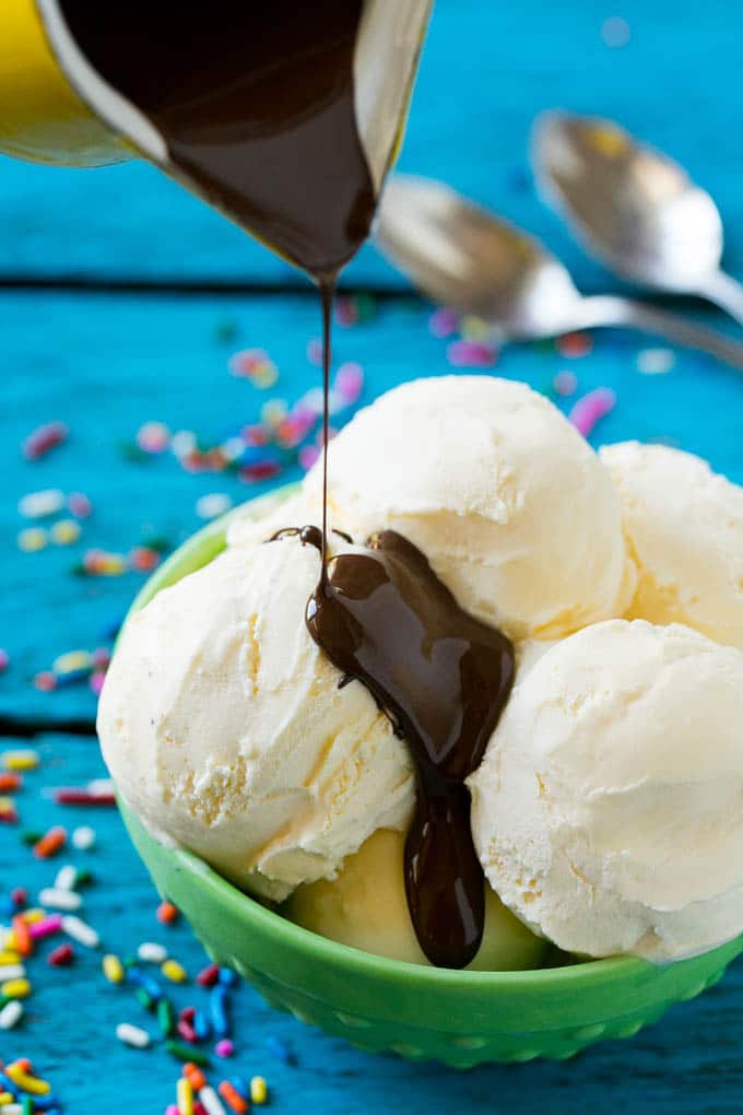 A pitcher of magic shell being poured over vanilla ice cream.