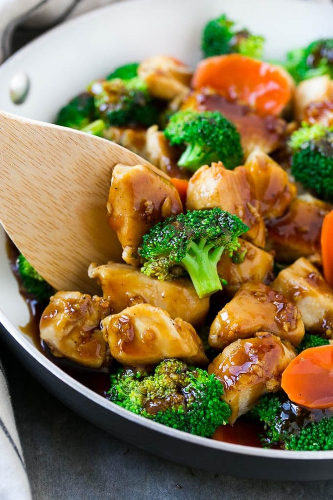 A skillet of honey garlic chicken stir fry with garlic, carrots and broccoli florets in a brown sauce.
