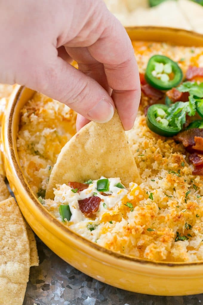 A hand scooping out a portion of jalapeno popper dip with a chip.