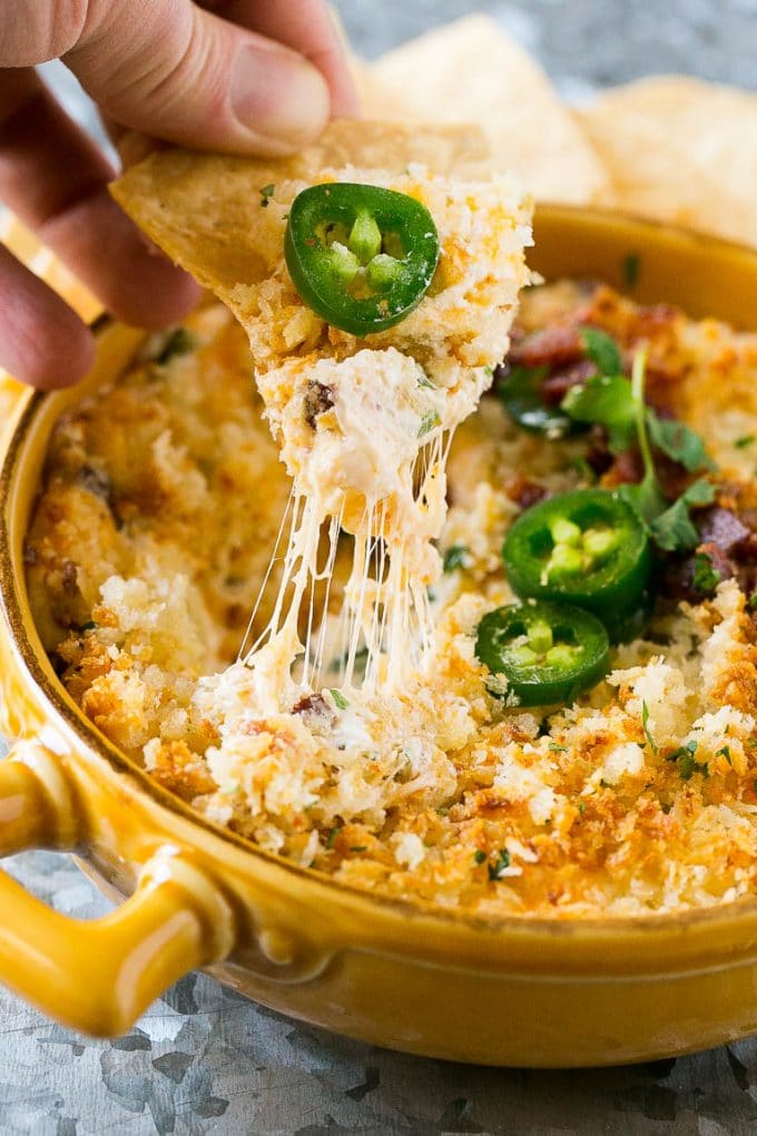 A hand scooping up a chip full of jalapeno popper dip.