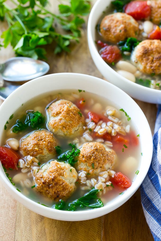Two bowls of farro soup with tomatoes, meatballs and kale.