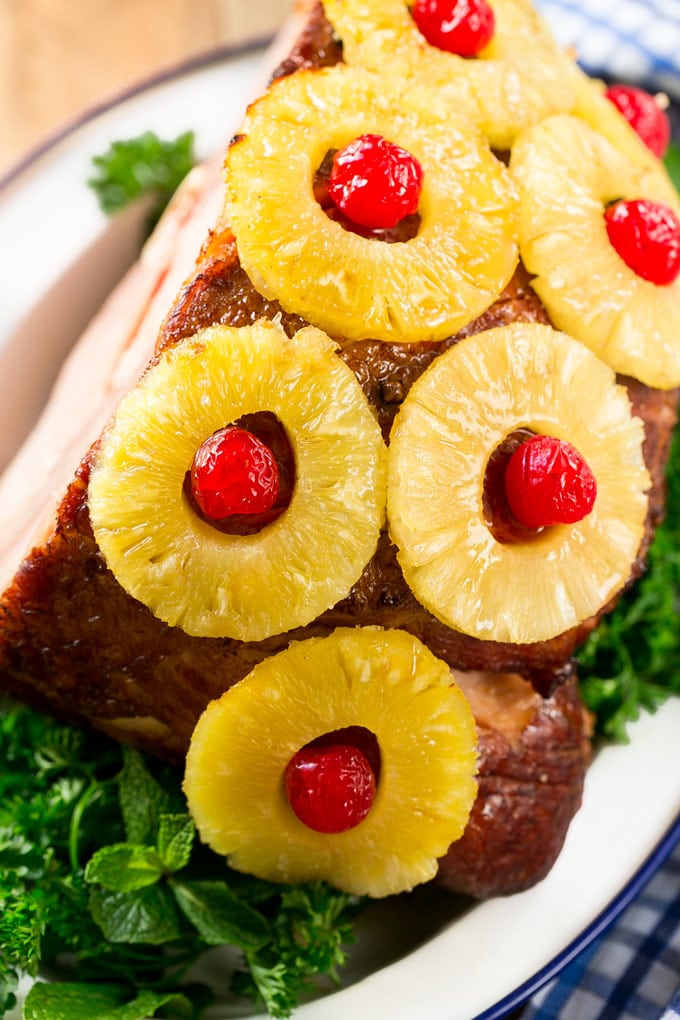 A close up of a ham covered in pineapple and cherries.
