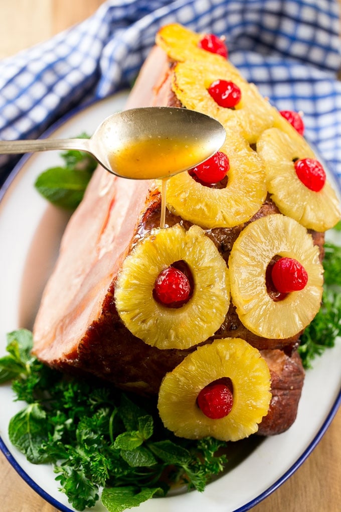 A spoon pouring glaze over a ham with pineapple and cherries.