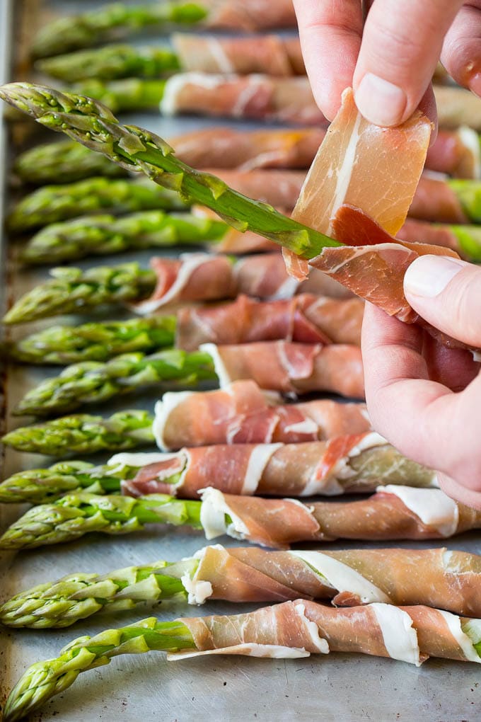 A hand wrapping a slice of meat around a stalk.