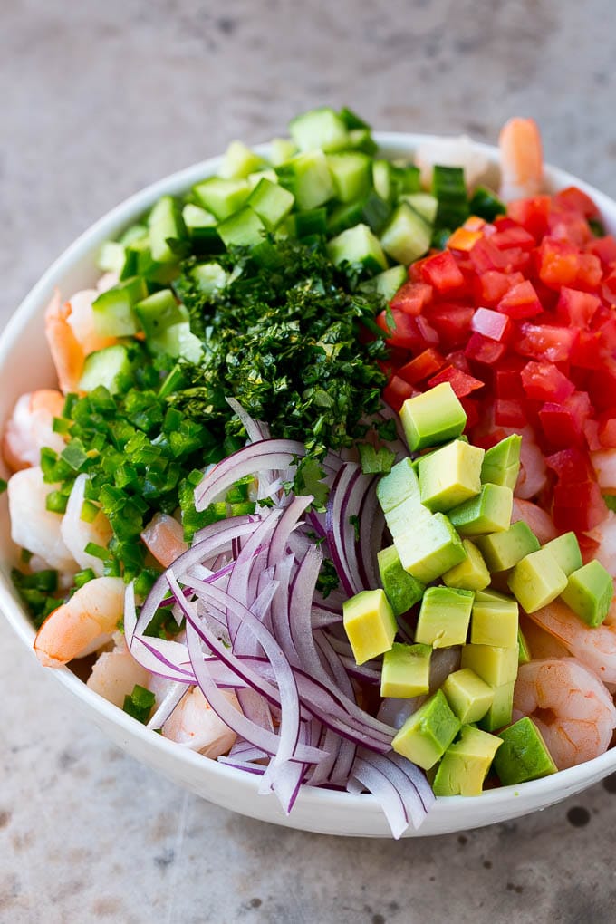 Prawns, avocado, red onion tomatoes, cilantro, jalapeno and cilantro in a bowl.