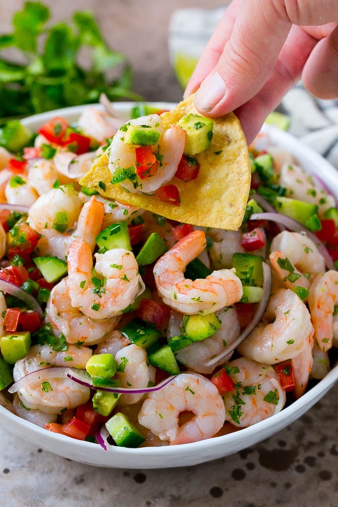 A bowl of shrimp ceviche with a tortilla chip scooping some out.