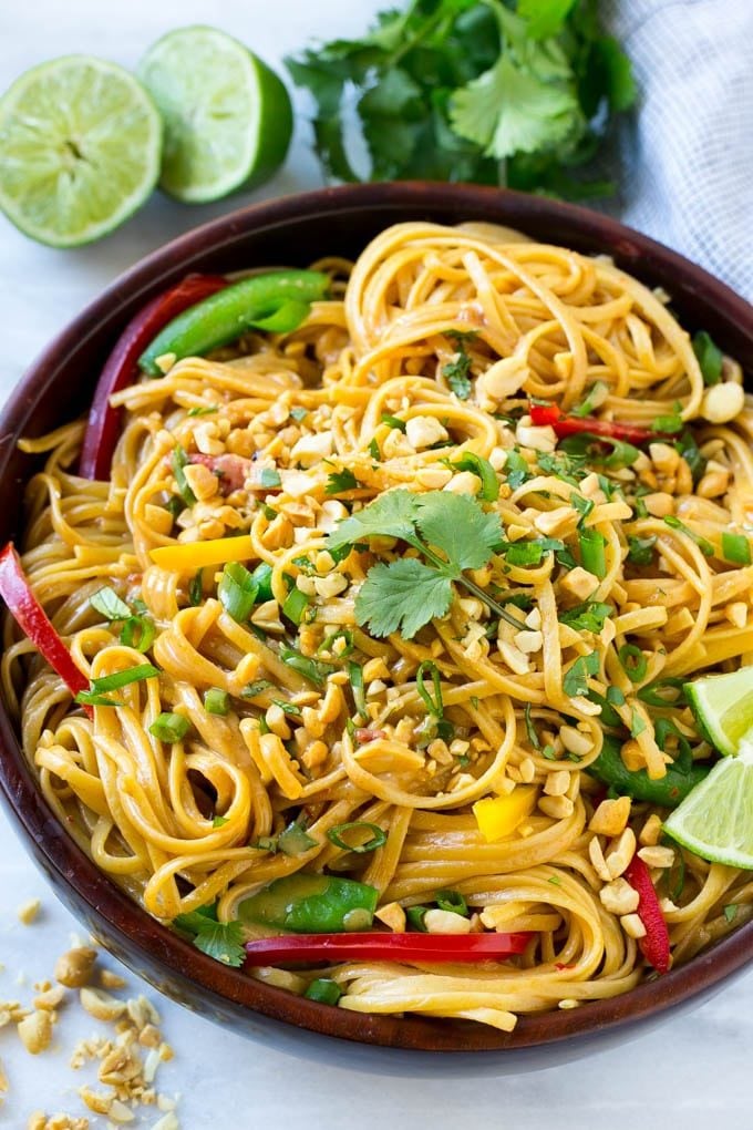 A serving bowl of Thai peanut noodles topped with fresh vegetables, chopped peanuts and herbs.