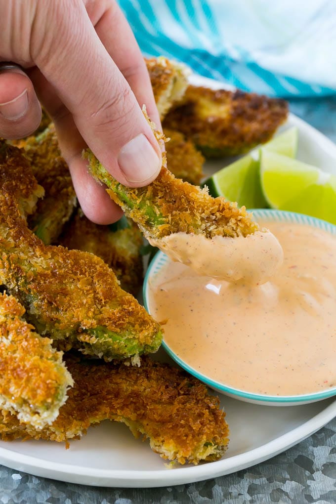 A hand dipping an avocado fry into sauce.