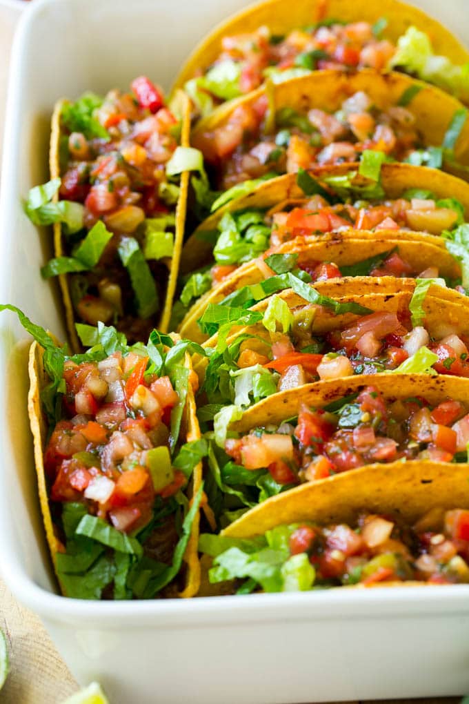 A pan full of baked beef tacos topped with salsa and lettuce.