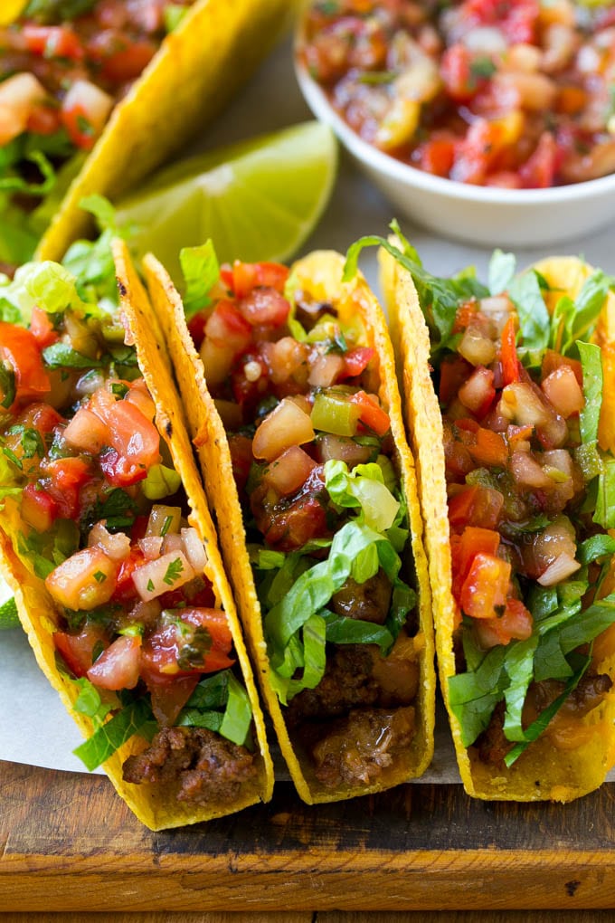 Three baked beef tacos topped with lettuce and salsa.