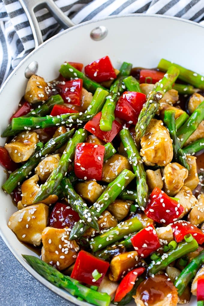 A pan of chicken teriyaki stir fry with chicken pieces, asparagus and red peppers.