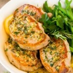 Baked boneless pork chops in a serving platter with herbs and green beans.