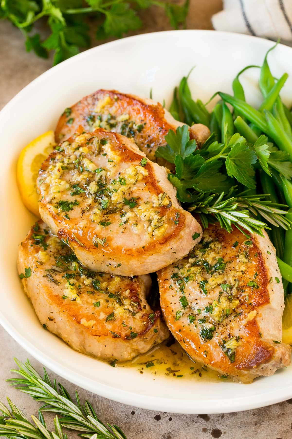 Baked boneless pork chops in a serving platter with herbs and green beans.