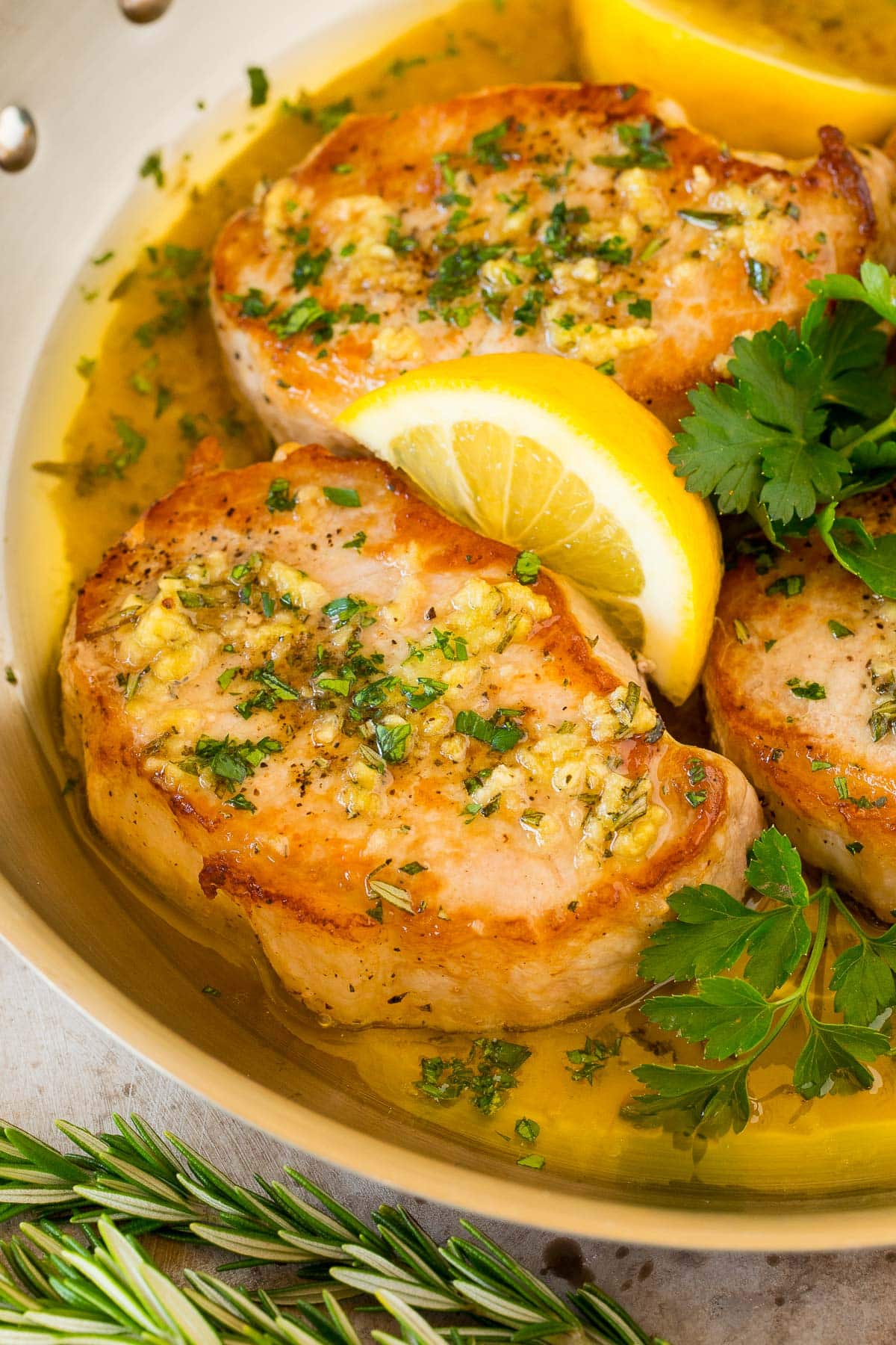 Baked boneless pork chops in a pan with lemon and parsley.