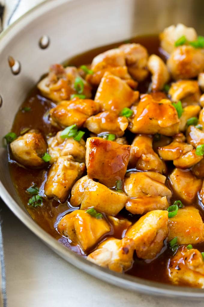 Bourbon chicken in a skillet coated in sauce and topped with green onions.