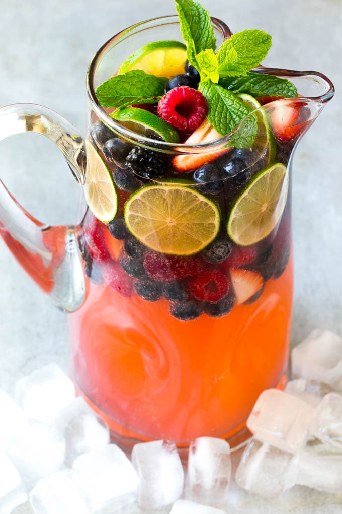 A pitcher of a cocktail garnished with fruit and mint.