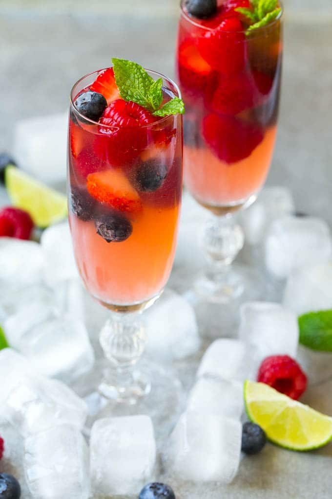 A glass pitcher filled with berry champagne punch garnished with lime.