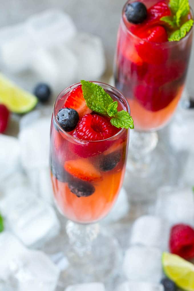 Two glasses of refreshing champagne punch with berries and mint on top.