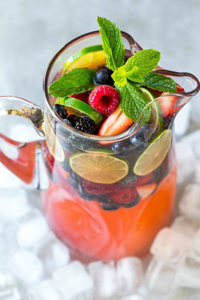 A pitcher of champagne punch filled with fresh berries and mint sprigs.