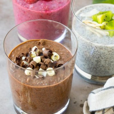 Three cups of chia pudding topped with chocolate and fruit, then garnished with mint.