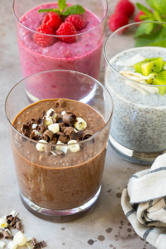 Three cups of chia pudding topped with chocolate and fruit, then garnished with mint.