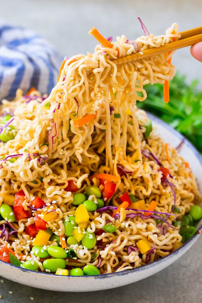 Chopsticks picking up noodles in a vegetable salad.