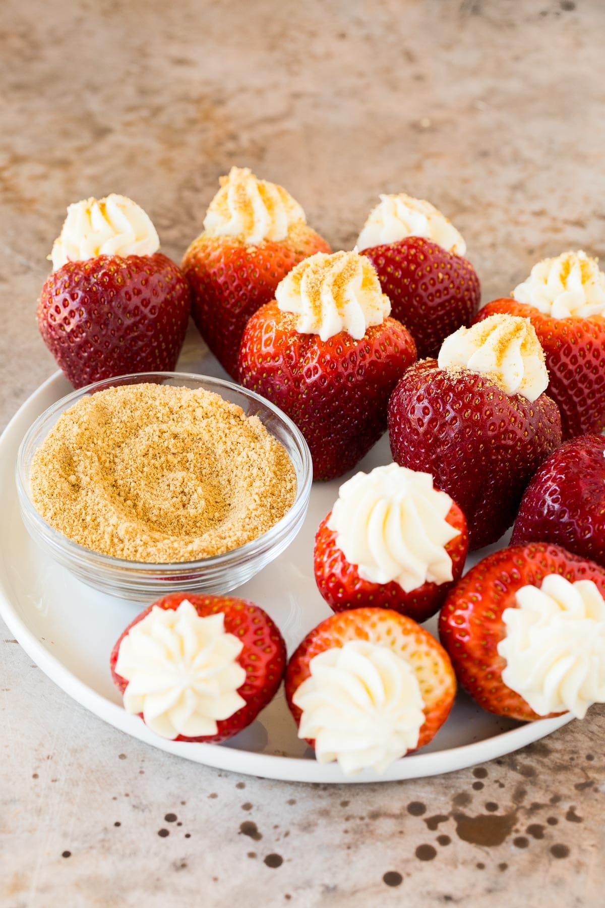 Berries stuffed with cream cheese on a plate with a bowl of graham cracker crumbs.