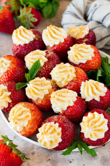 A plate of cheesecake stuffed strawberries garnished with fresh mint.