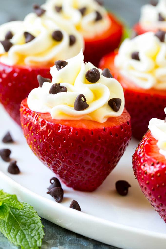 Cheesecake stuffed strawberries on a serving plate, garnished with miniature chocolate chips.