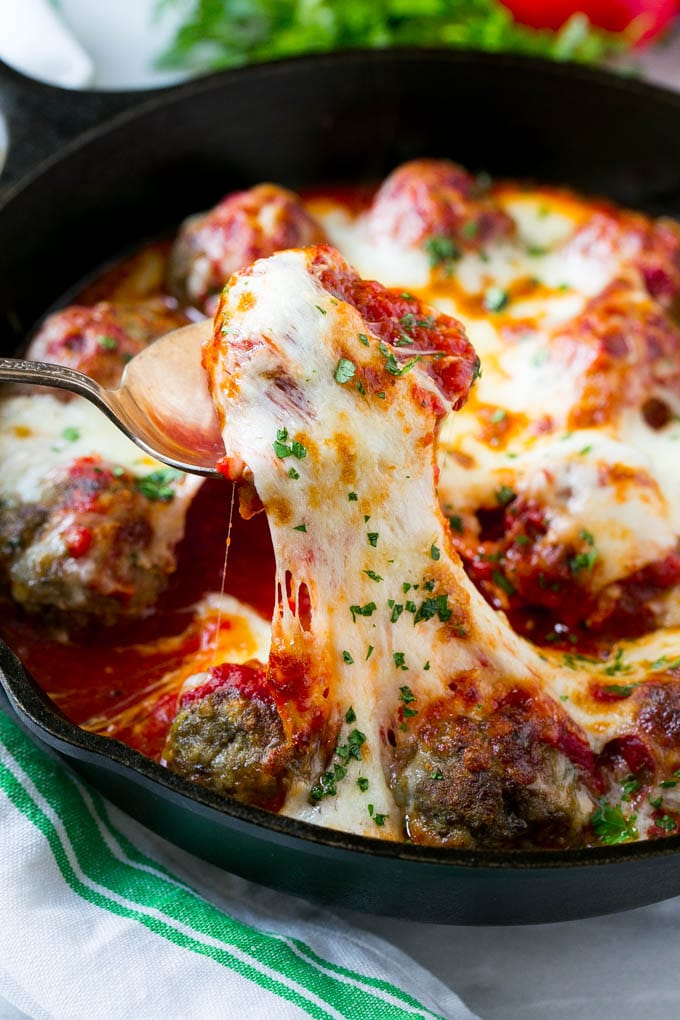A serving spoon in a pan of cheesy meatball bake.