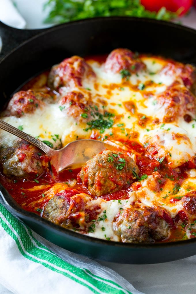 A serving spoon in a skillet of meatball bake, topped with chopped parsley.