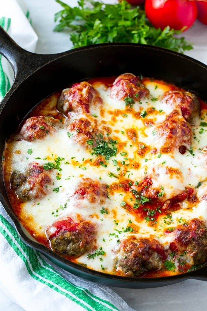 A skillet of baked meatballs with tomato sauce and melted cheese.