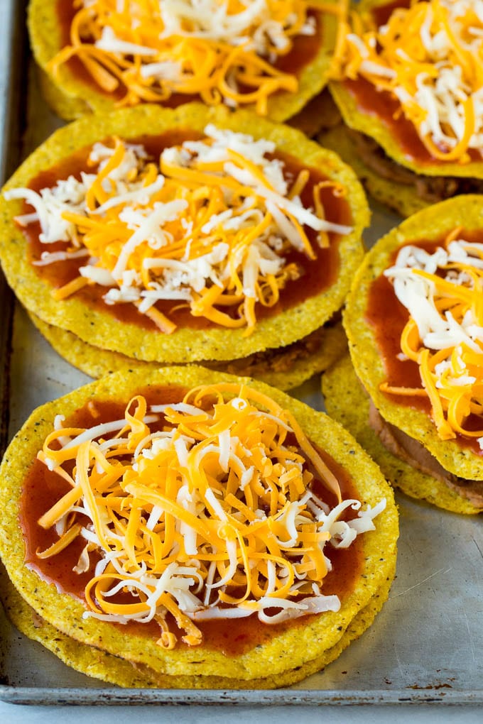 Layered tostadas topped with enchilada sauce and shredded cheese.