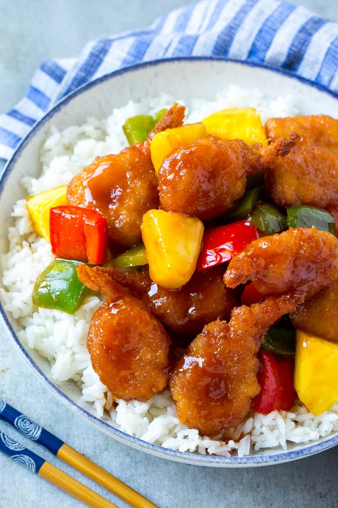 A bowl of rice with sweet and sour shrimp, vegetables and pineapple chunks.