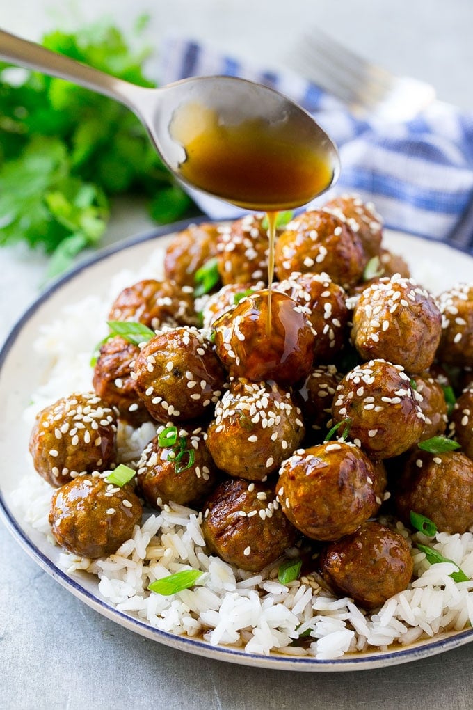 Teriyaki sauce spooned over a pile of meatballs on a bed of rice.