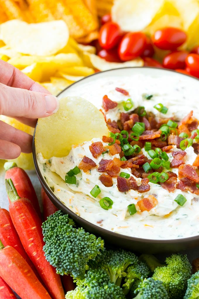 A hand scooping up bacon ranch dip with a potato chip.
