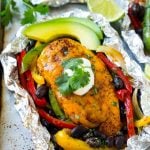 Cooked chicken breasts covered in cheese surrounded by peppers, onions and black beans, all inside a foil packet.