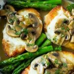 Cooked chicken breasts in a stainless steel pan, topped with melted cheese and mushroom sauce.