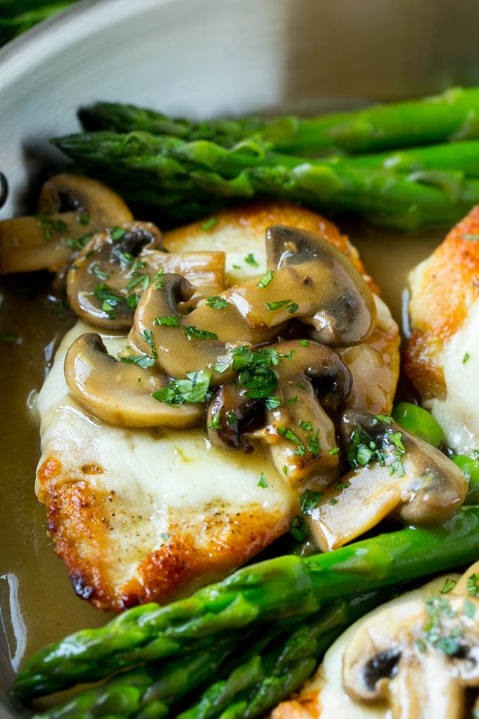 A chicken breast topped with mozzarella cheese and madeira mushroom sauce in a pan.