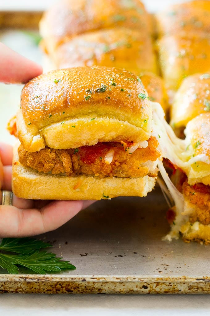 A crispy chicken parmesan slider being pulled away by a hand.