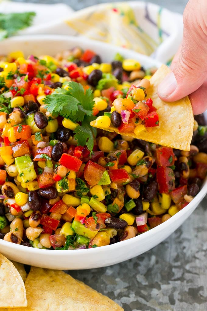 A bowl of cowboy caviar with a hand holding a chip topped with this dip.