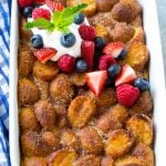 A tray of donut bread pudding garnished with whipped cream and berries.