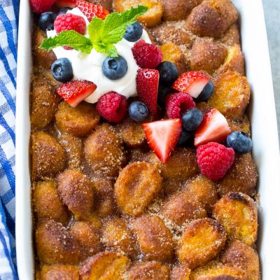A tray of donut bread pudding garnished with whipped cream and berries.