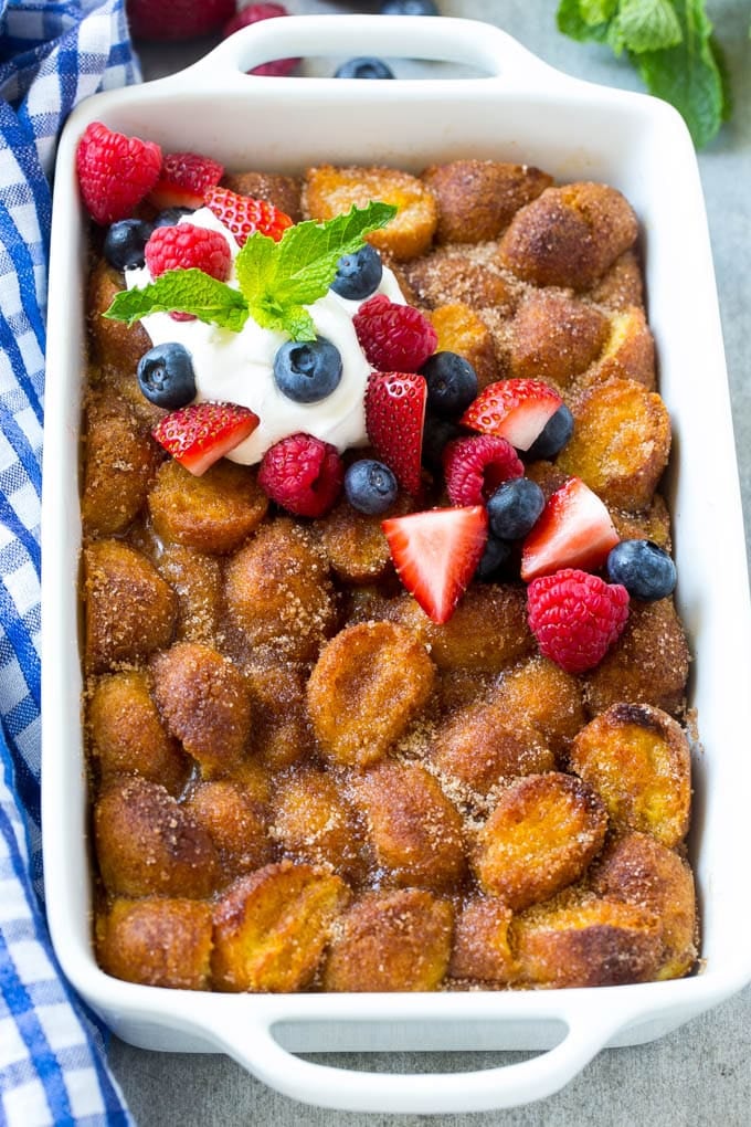 A tray of donut bread pudding garnished with whipped cream and berries.