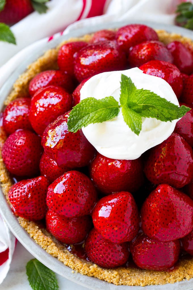 Overhead view of a strawberry pie with whipped cream and a mint garnish.