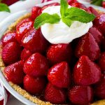 A pile of strawberries inside a graham cracker crust, topped with a shiny red glaze, whipped cream and mint.