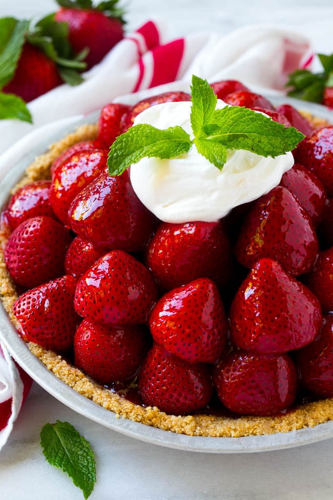 Strawberry pie with a pile of strawberries inside a graham cracker crust, topped with glaze and whipped cream.