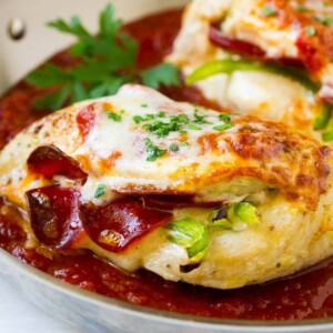 Chicken breasts stuffed with pepperoni and cheese in a pan of marinara sauce.