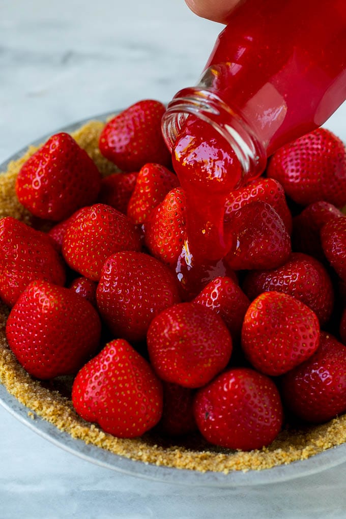 Glaze being poured over a strawberry pie.