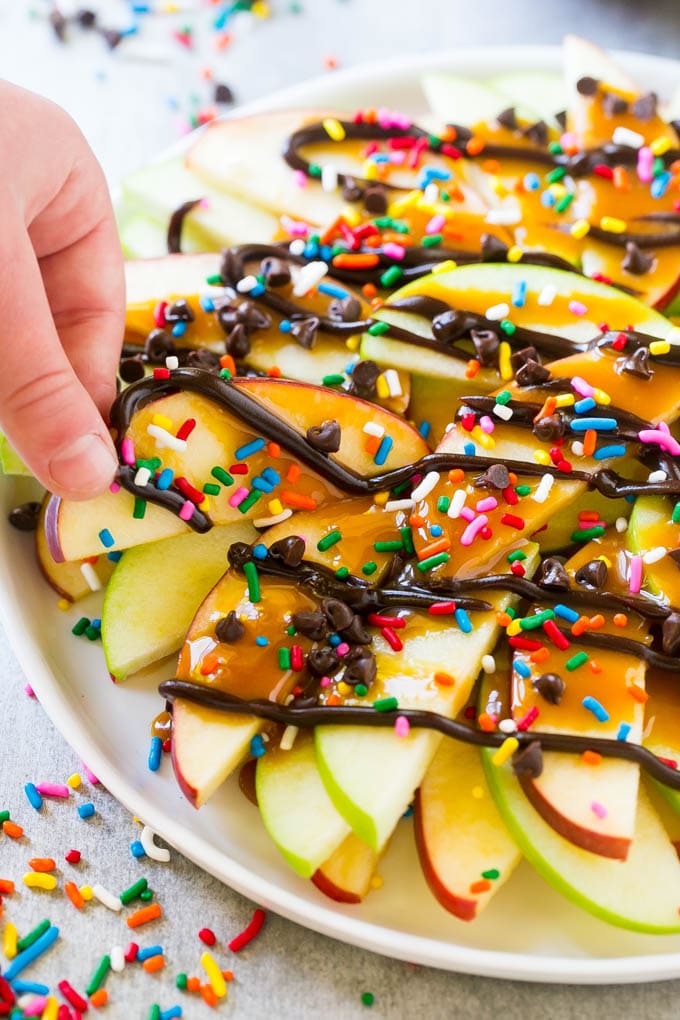 A plate of caramel apple nachos with a hand reaching out to take one.